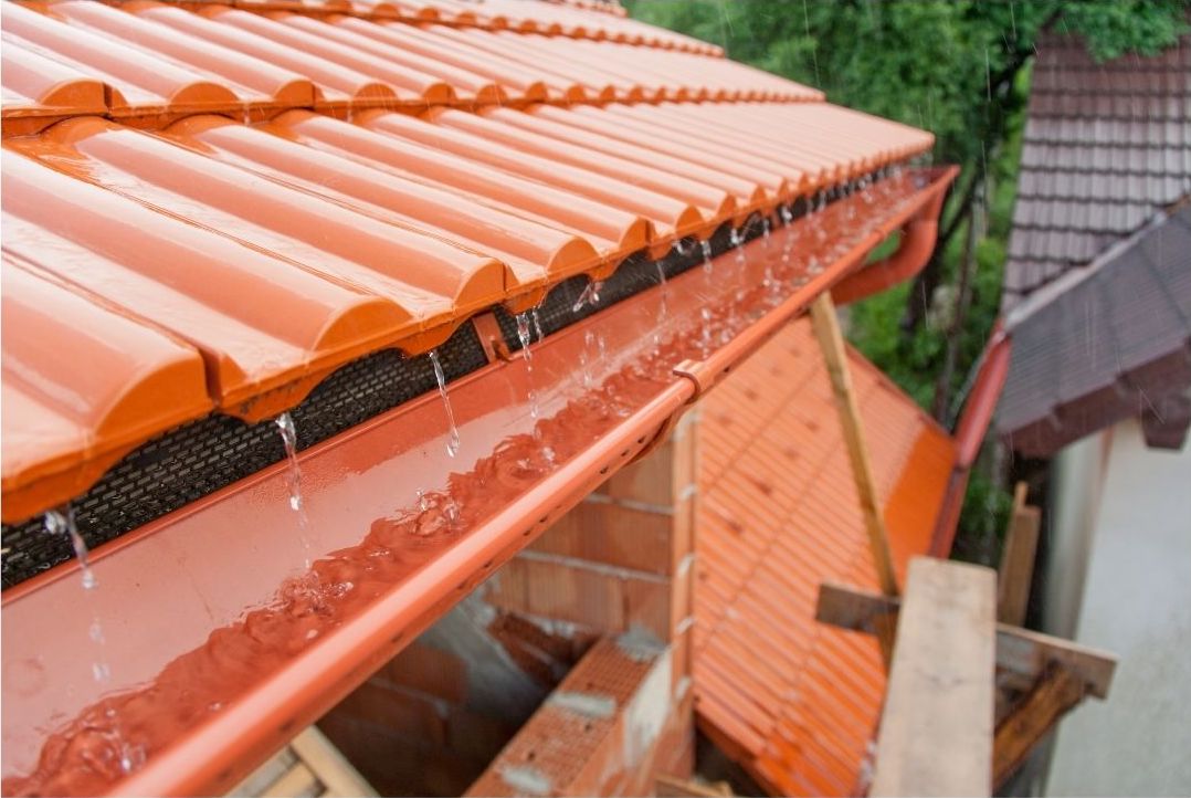 A brand new orange roof gutter. Rain is dripping from orange roof tiles into the gutter and is being carried away to the drain.